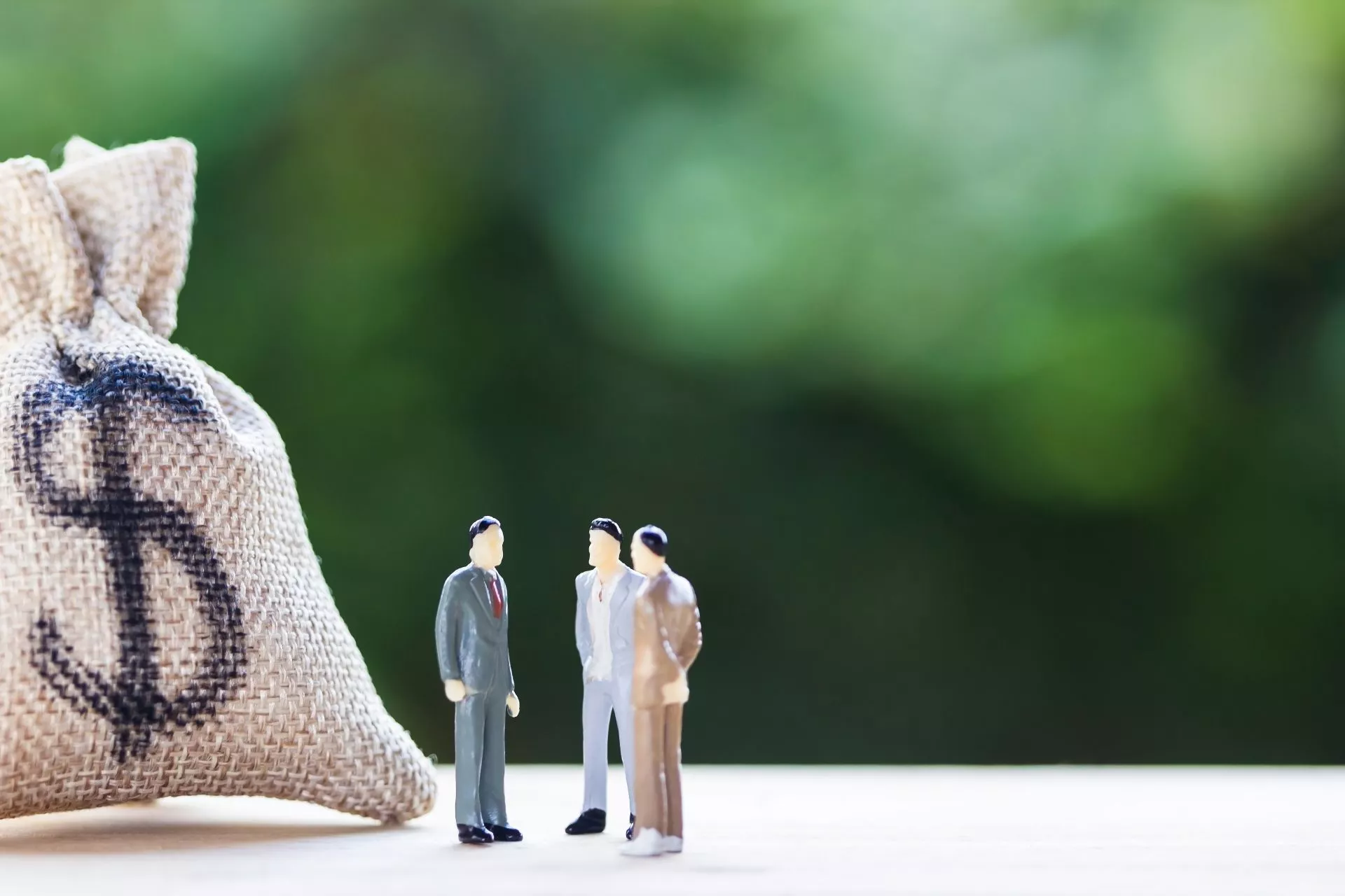 三個商務人士模型站在裝有金錢符號的布袋旁討論資金規劃，象徵資金周轉與借款評估情境，代表台中當鋪提供的汽車借款與資金周轉服務。